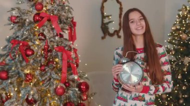 Süslü bir Noel ağacının yanında çalar saati tutan gülümseyen kız. Noel ağacının yanında saati olan kız, Noel ağacının yanında saati olan kız..
