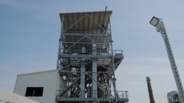 Endüstriyel tahıl ambarları ve işleme tesisi. Kırsal kesimde açık mavi gökyüzünün altında birden fazla metal tanecikli siloları ve karmaşık boru tesisleri olan büyük bir sanayi tesisi.