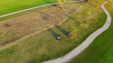 Lush Green Pisti 'nde golf arabaları ve golf arabaları. Yeşil golf sahasında at arabalarıyla gezen golfçülerin hava manzarası, dolambaçlı yollar, çimenli arazi ve ağaçlar.