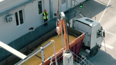 Tesisteki bir kamyona tahıl yükleyen işçiler. Güvenlik yeleği ve kask giyen bir işçi büyük bir kamyona yüklenen tahıl işlemini denetliyor.