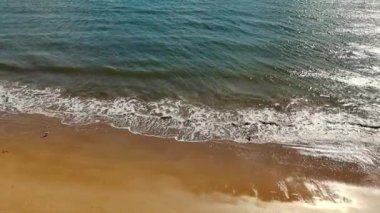 Dalgalar yavaşça kumsala ulaşıyor. Kumlu kıyı şeridinde süzülen küçük dalgaların yakın görüntüsü, parlak güneş ışığı altında ışıldayan su huzur verici bir sahne yaratır.