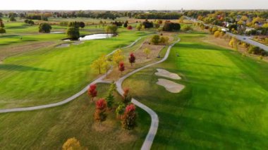 Sonbaharda Havadan Manzaralı Golf Sahası. Geniş golf sahası yemyeşil çayırları, kum sığınakları, dolambaçlı yollar ve güneşli bir gökyüzünün altında renkli sonbahar ağaçları.