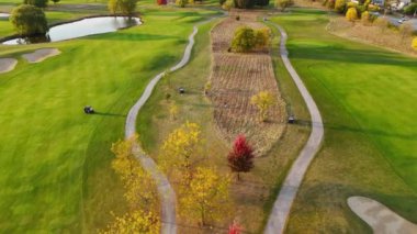 Sonbahar ağaçları ve patikaları olan bir golf sahasının havadan görünüşü canlı bir hava manzarası yemyeşil otlar, dolambaçlı yollar ve renkli sonbahar ağaçlarıyla dolu bir golf sahasını gösteriyor.