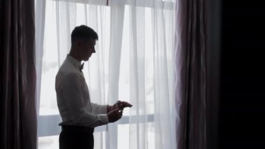 Pencere kenarındaki seyir saati, resmi kıyafet giyen siluetli damat saatini pencere kenarına ayarlar..