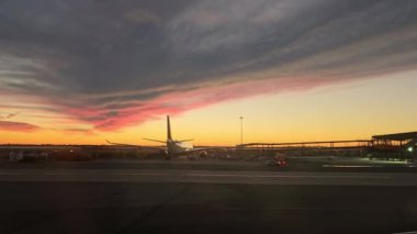 Runway 'de Sunset' te bir uçak, gün batımında canlı bir gökyüzünün altında piste park etmiş sakin bir uçağın görüntüsü.