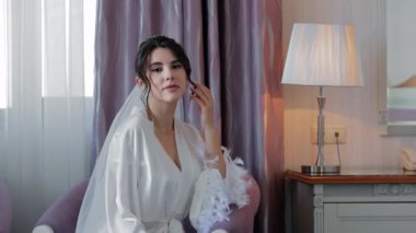 Düğünden önce beyaz cüppeli zarif bir gelin, beyaz saten bir bornoz ve duvak giyen güzel bir gelin, rahat bir odada oturuyor..