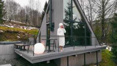 Kadın kışın Balkonda dinleniyor, kahve içiyor ve huzurlu kış manzarasının tadını çıkarıyor.