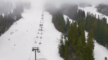 Sandalyeli kayak yamacı ve sisli orman, Yoğun ormanlarla çevrili bir kayak yamacı yukarıdan görülüyor.