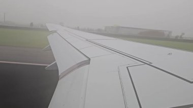 Uçak yoğun siste kalkıyor. Uçak bulutlu bir havaalanında pist boyunca ilerlerken kanadını gösteren bir uçak görüntüsü.