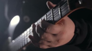 Elektro gitar akorları çalan bir elin yakın çekimi, müzisyenler elektro gitar ensesinde tellere basıyorlar.
