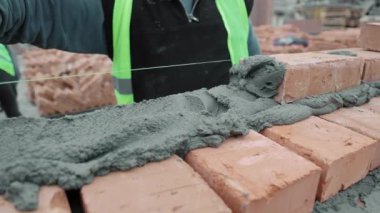 İnşaat alanında harç ve tuğla hizalayan işçiler, tuğlalara harç döşeyen ve hizalayan işçilere yakın çekim