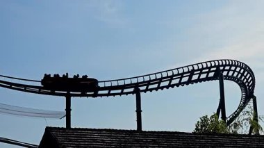 Lunaparktaki masmavi gökyüzüne karşı lunaparktaki roller coaster silueti, gökyüzüne doğru yükselirken, siluette yakalanan heyecan verici lunapark treni..