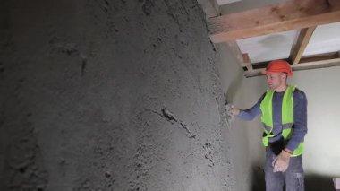 İnşaat işçisi duvarın yüzeyini alçılıyor, işçiler binanın içindeki bir duvara alçı yapıştırıyor..