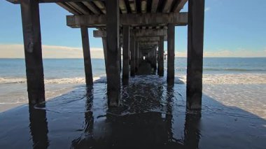 Okyanus rıhtımının altında, sakin su yansımalarıyla, yukarıdaki yapıyı yansıtan okyanus dalgaları olan bir rıhtım manzarası.