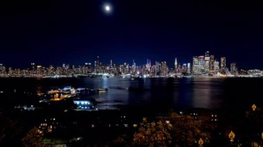 Manhattan siluetinin ay ışığı altında parlaması Hudson Nehri 'ne yansıyor. Iconic Manhattan silueti, Hudson Nehri' ne yansıyan ay ışığıyla hızlandırılmış bir zaman çizgisi.