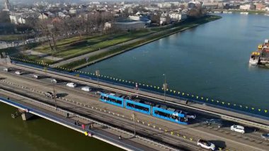 Krakow Polonya 03.02.2025 Krakow, Polonya 'daki Vistula Nehri üzerinden geçen bir tramvayın hava görüntüsü, Vistula Nehri üzerindeki manzaralı park alanlarına sahip bir köprüden geçen mavi tramvay ve araçlar.