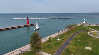 Yelkenli ve renkli deniz fenerli marina güneşli bir günde Kenosha, Wisconsin 'de, yeşil park alanları ve asfalt yollarla çevrili bir marinanın yakınındaki kırmızı bir deniz fenerinin yanından geçiyor.