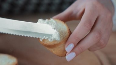 Kızarmış ekmeğin üzerine yumuşak peynir serpiştirmek, bir bıçağın yakın planında kızarmış ekmeğin üzerine yumuşak peynir sürmek.