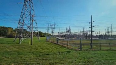 Çimenli alanla çevrili açık mavi gökyüzünün altında elektrik santrali ve elektrik hatları.