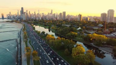 Chicago şehir manzarası gün batımında trafik var. Gün batımında Chicago 'nun gökyüzü manzarası. Lake Shore Drive boyunca trafik, ağaçlar ve sıcak sonbahar renklerini yansıtan su.