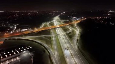 Gece aydınlık otoyol kavşağının havadan görünüşü, arka planda akan trafik ve şehir ışıkları