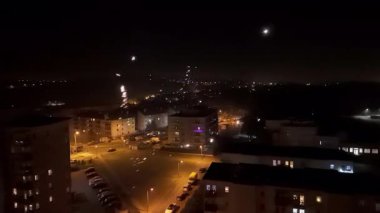 Gece vakti havai fişekler bir yerleşim alanı üzerinde, binaları ve sokakları aydınlatıyor.
