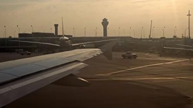 Gün batımında havaalanı, uzaktaki bir uçak penceresinden, uçaklardan ve terminallerden manzara.