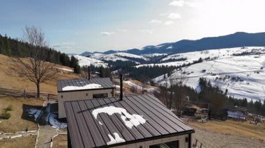 Etrafı karlı tepeler ve nefes kesici panoramik manzaralarla çevrili metal çatıları olan modern dağ kulübeleri..