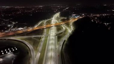 Gece aydınlanan otoyol kavşağı, ışık yolları ve şehir manzaralı modern yol altyapısının havadan görünüşü, hareket halindeki kentsel ulaşım ağı
