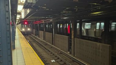 - New York. Biziz. 03.03.2025 New York metro treni yeraltı platformuna yaklaşıyor. İkonik tasarım, floresan aydınlatma ve kumlu atmosfer ile kentsel ulaşım sistemi sergileniyor..