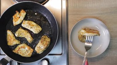 Tavada tavada kızaran ızgara tavuk filetolarının üst görüntüsü bir çatalla servis edilen tabağın yanında, yemek pişirme ve servis etme arasında kontrastlık gösteriyor.