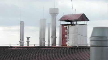 Kırmızı metal çatılı sanayi bacası, bulutlu bir günde çoklu çelik havalandırma borularının yanında hafif duman yayar.