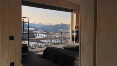 Panoramik dağ manzaralı manzara odası, karlı dağlar ve tepelere bakan geniş pencereli ahşap yatak odası.