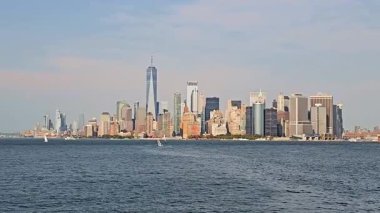 Hudson Nehri boyunca uzanan Manhattan 'ın panoramik manzarası, modern ve tarihi gökdelenler, yumuşak gün ışığı altında suyla parlayan tekneler.