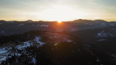 Dağ vadisinde altın kış günbatımı, karla kaplı bir dağ sırasının üzerinde sersemletici gün batımı..