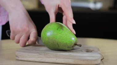 Olgun yeşil armudu ahşap kesim tahtasında lekelerle dilimleyen kadın doğal meyve kusurlarını, ev hazırlıklarını ve dikkatli yemek seçimlerini vurguluyor.