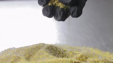 Siyah eldivenli el, altın elmas aşındırıcı tozu yansıtıcı bir yüzeye düşürüyor. Makro görünüm, alet üretimi sırasında kontrollü madde kullanımı.