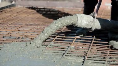 Endüstriyel hortumdan güçlendirilmiş inşaat demiri şebekesine beton dökülüyor, ıslak çimento karışımı inşaatın ilk safhalarında temel plakası oluşturmak için yayılıyor.
