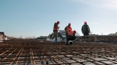 Temiz mavi gökyüzü altında temel hazırlıkları sırasında inşaat alanında inşaat işçileri inşaat demirleri ve beton hortumlarla çalışıyor.