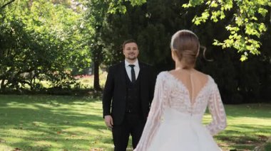 Gelin, ağaçlarla çevrili yeşil çimlerde damada doğru koşuyor, romantik ilk bakışta düğün anı orman bahçesinde doğal güneş ışığı ile birlikte.
