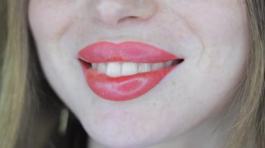 Gülümseyen, yeni yapılmış dudak makyajlı, yumuşak pembe gözlükleri olan ve stüdyo ışıkları altında doğal deri dokusu olan bir kadının yakın çekimi.