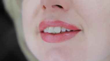 Yumuşak pembe makyajlı kadın dudakları, gün ışığında doğal şekli, parlaklığı ve pürüzsüz cilt dokusunu, narin gülüşü olan stüdyo ortamında gösteriyor.