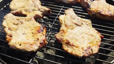 Kömür ızgarasında cızırdayan leziz domuz pirzolası görünür duman ve altın kabuk, yaz pikniği sırasında açık hava barbekü sahnesinin yakın çekimi
