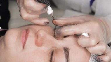 Kalıcı kirpik çizgisi dövme prosedürü devam etmekte, kozmetikçi yakın çekim sırasında profesyonel dövme cihazı kullanarak kirpiklerin arasında pigment uygular