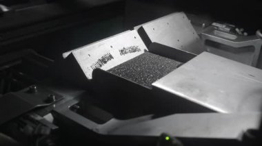 Endüstriyel titreşim tepsisindeki küçük siyah tanecikler, otomatik sıralama makinesi işlemi.