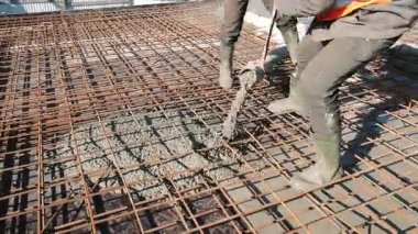 Çelik inşaat iskeletine beton dökülüyor, inşaat alanında lastik çizmeli işçiler.