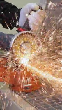 Açı öğütücüsüyle metal kesen işçiler parlak kıvılcımlar üretiyor. Endüstriyel üretim sırasında elektrikli aletler kullanan inşaat işçilerinin yakın plan güvenlik eldivenleri.