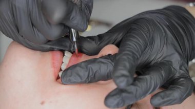 Siyah eldivenli güzellik uzmanı dudak dövmesi ameliyatı yapıyor, kırmızı pigmentlere iğne batırıyor..