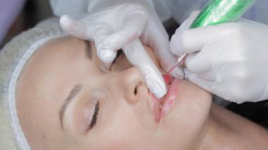 Kalıcı dudak makyajı prosedürü devam ediyor, eldivenli güzellik uzmanı hassas bir aletle pigment uyguluyor..