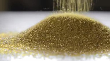 Altın aşındırıcı parçacıklar yığının içine düşüyor, kumlama ve filtreleme işlemlerinde kullanılan endüstriyel maddelerin yakın görüntüsü.